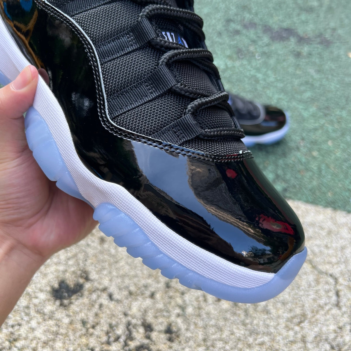 Nike Air Jordan 11 Retro Space Jam sneakers in black patent leather with icy blue outsole, front view showing iconic design details.
