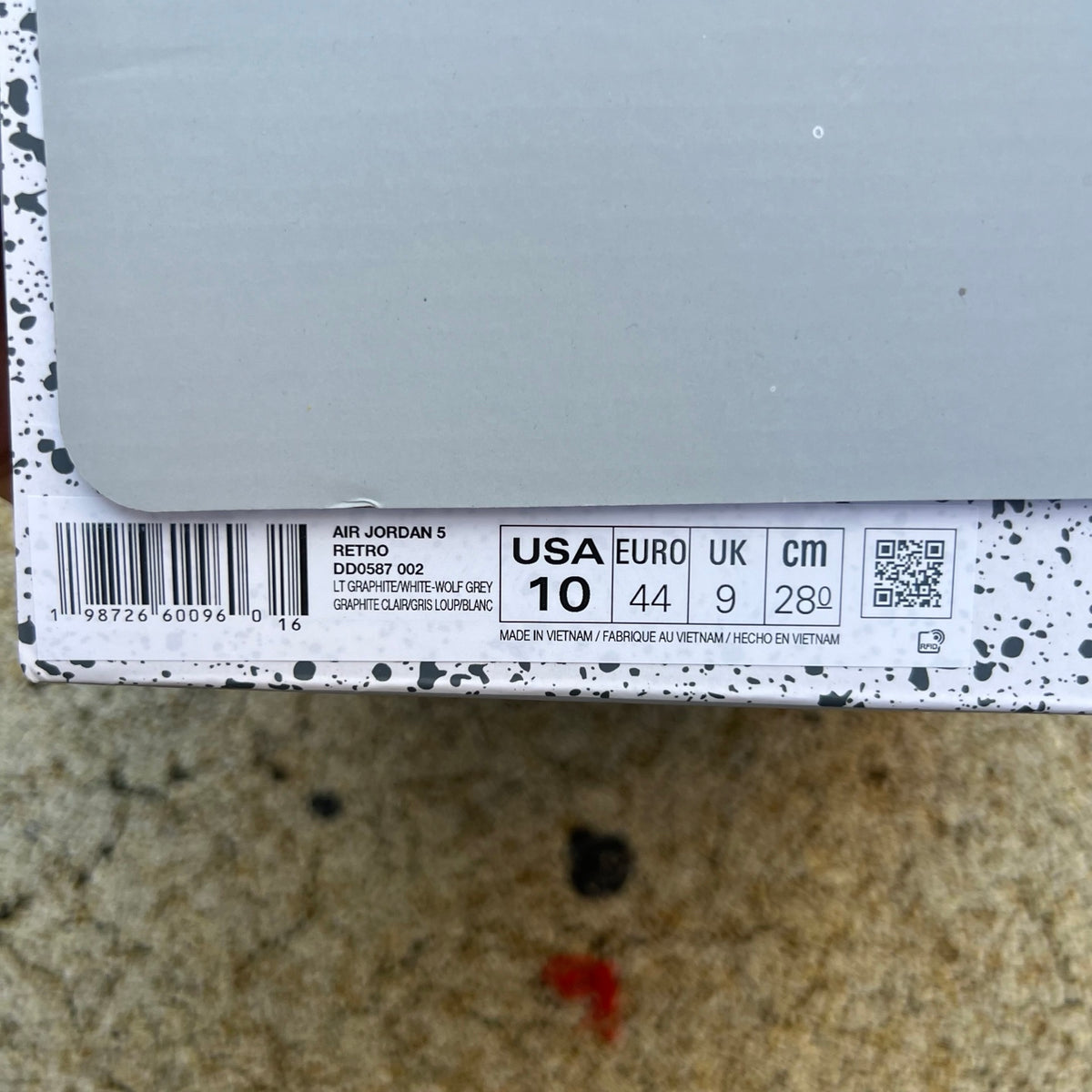 Nike Air Jordan 5 Retro Wolf Grey sneakers showing the side view with grey leather and red accents, branded with Nike and Jordan logos.