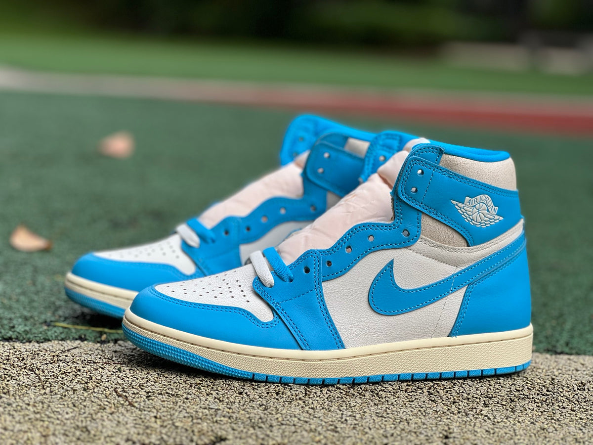 Nike Air Jordan 1 Retro High OG UNC Reimagined sneakers in white and blue leather with Nike and Jordan branding.