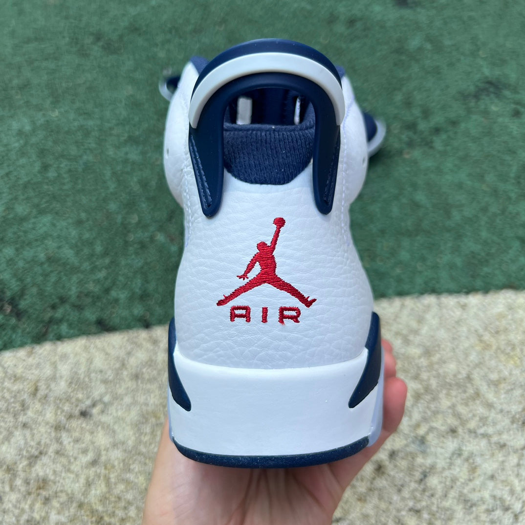Nike Air Jordan 6 Retro Olympic sneakers in white, blue, and gold colorway with Nike and Jordan branding, displayed from a side angle.
